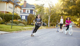 Three pre-teen girls playing in street on scooters and bike