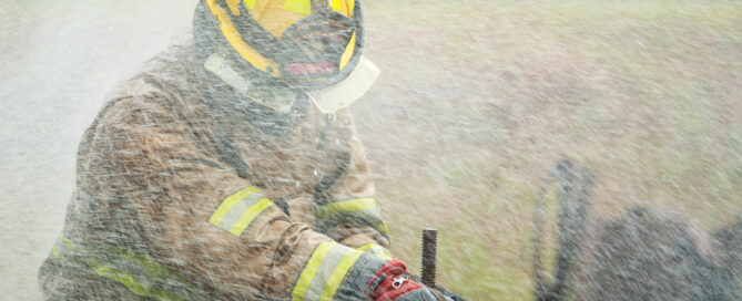 Close up action shot of firefighter's gloved hands operating a metal water valve during training. Amidst spray and smoke. Physical intensity and mechanical precision of fire suppression operations.